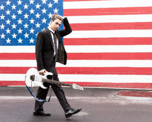 Walking with guitar in front of American Flag